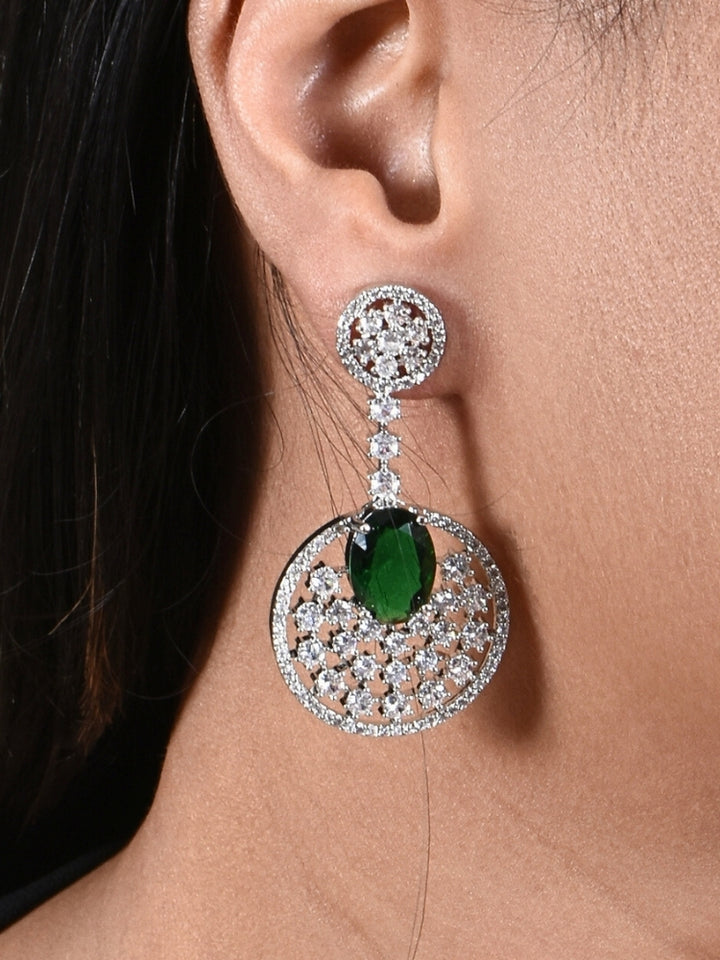 Close-up of a woman wearing an ornate Western (Silver Polish) Green Diamond Earrings with American Diamond and Colored Stones. Bride wearing luxury artificial American Diamond earrings for reception night. Reception-ready look completed with statement artificial jewelry American Diamond earrings.