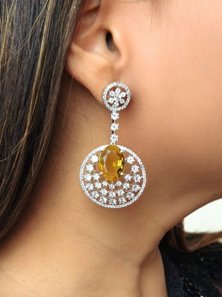 Close-up of a woman wearing an ornate Western (Silver Polish) Yellow Diamond Earrings with American Diamond and Colored Stones. Bride wearing luxury artificial American Diamond earrings for reception night. Reception-ready look completed with statement artificial jewelry American Diamond earrings.