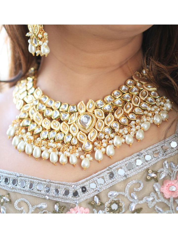 Close-up of a woman wearing an ornate traditional Gold Collar Necklace set, Eaarings and Mangtikka with Kundan, Pearls and American Diamonds. Bride wearing a traditional Kundan artificial necklace set for her wedding ceremony. Royal bridal look featuring a traditional Kundan necklace set.