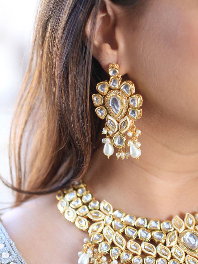 Close-up of a woman wearing an ornate traditional Gold Collar Necklace set, Eaarings and Mangtikka with Kundan, Pearls and American Diamonds. Bride wearing a traditional Kundan artificial necklace set for her wedding ceremony. Royal bridal look featuring a traditional Kundan necklace set.