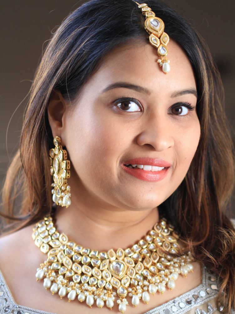Close-up of a woman wearing an ornate traditional Gold Collar Necklace set, Eaarings and Mangtikka with Kundan, Pearls and American Diamonds. Bride wearing a traditional Kundan artificial necklace set for her wedding ceremony. Royal bridal look featuring a traditional Kundan necklace set.