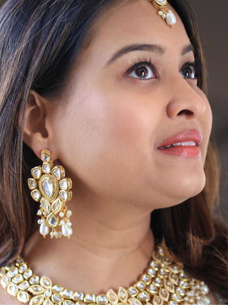 Close-up of a woman wearing an ornate traditional Gold Collar Necklace set, Eaarings and Mangtikka with Kundan, Pearls and American Diamonds. Bride wearing a traditional Kundan artificial necklace set for her wedding ceremony. Royal bridal look featuring a traditional Kundan necklace set.