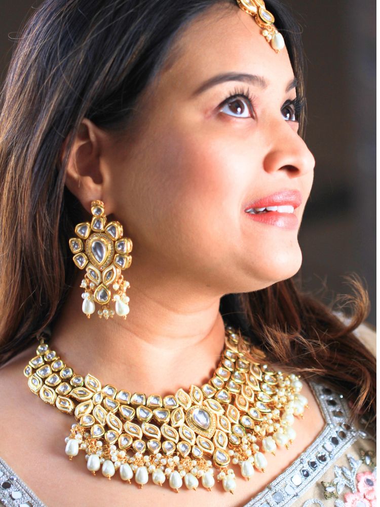 Close-up of a woman wearing an ornate traditional Gold Collar Necklace set, Eaarings and Mangtikka with Kundan, Pearls and American Diamonds. Bride wearing a traditional Kundan artificial necklace set for her wedding ceremony. Royal bridal look featuring a traditional Kundan necklace set.