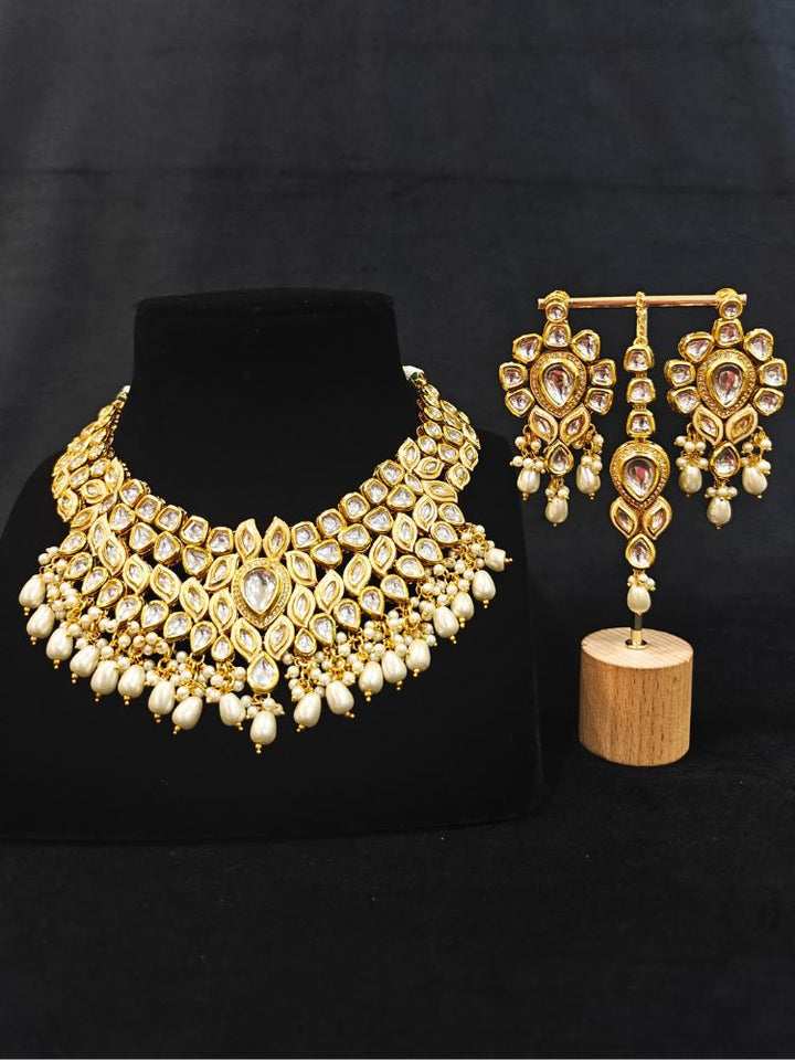 Close-up of an ornate traditional Gold Collar Necklace set, Eaarings and Mangtikka with Kundan, Pearls and American Diamonds. A traditional Kundan artificial necklace set for her wedding ceremony. Royal bridal look featuring a traditional Kundan necklace set.