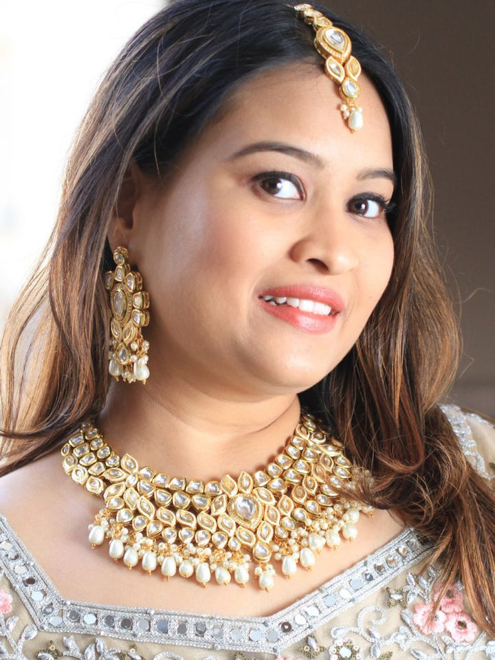 Close-up of a woman wearing an ornate traditional Gold Collar Necklace set, Eaarings and Mangtikka with Kundan, Pearls and American Diamonds. Bride wearing a traditional Kundan artificial necklace set for her wedding ceremony. Royal bridal look featuring a traditional Kundan necklace set.
