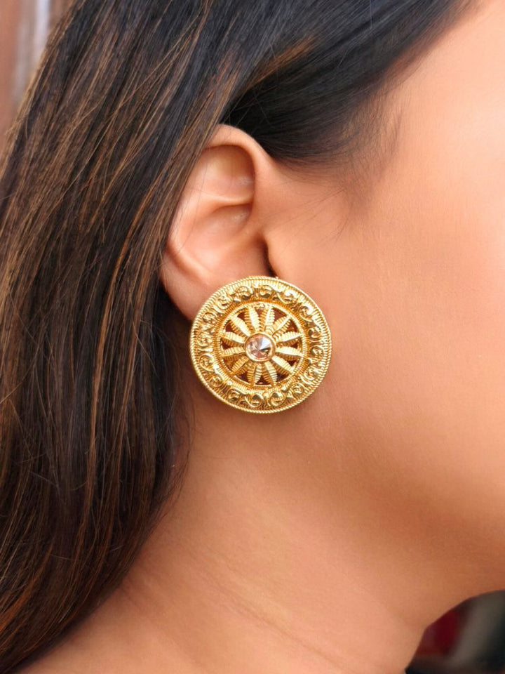 The Akhila Earrings are round gold stud earrings featuring a wheel shape design, with a central gemstone and Reverse American Diamond accents. Festive Diwali look styled with premium artificial Studs earrings. Close-up of anti-tarnish artificial Studs earrings for festive celebrations.