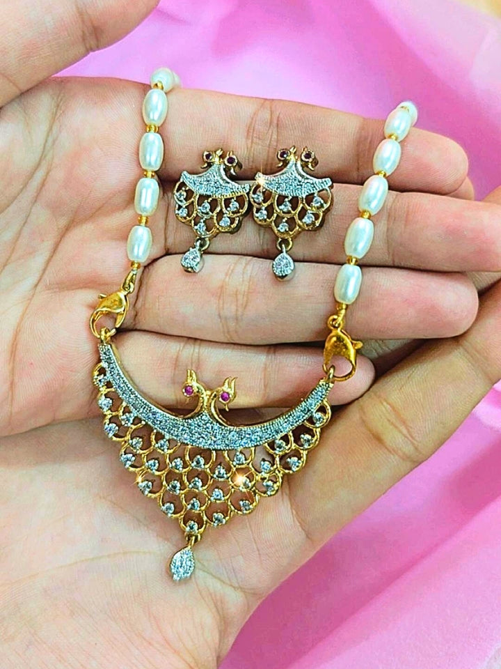 A hand holds the Akshita Mangalsutra—a gold necklace with black mangalsutra beads and matching earrings, pendant featuring sparkling American Diamonds—set against a soft pink background, perfect for your wedding ceremony dress. Diamond mangalsutra. Modern mangalsutra. 