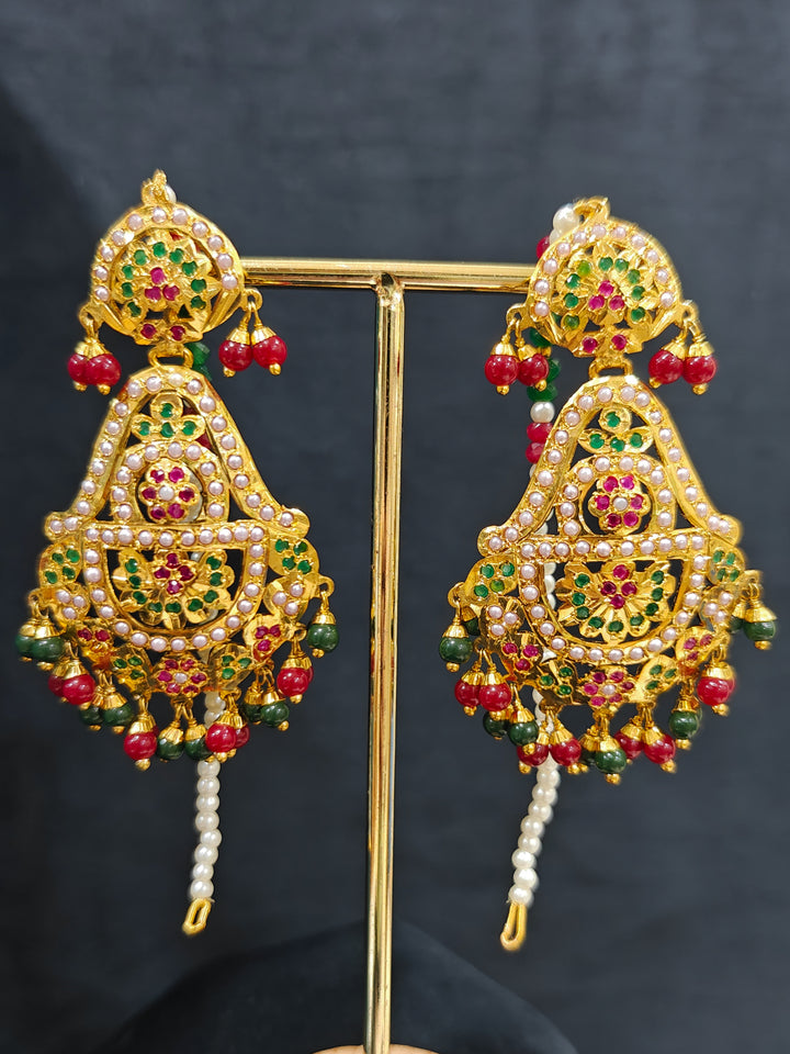 Closeup of an ornate traditional Long jadau gold jewellery set and  jadau earrings and maangtikka with crystals beads and gemstones. Wedding guest styling a long Jadau artificial necklace. Jadau necklace styled for a wedding guest outfit.

