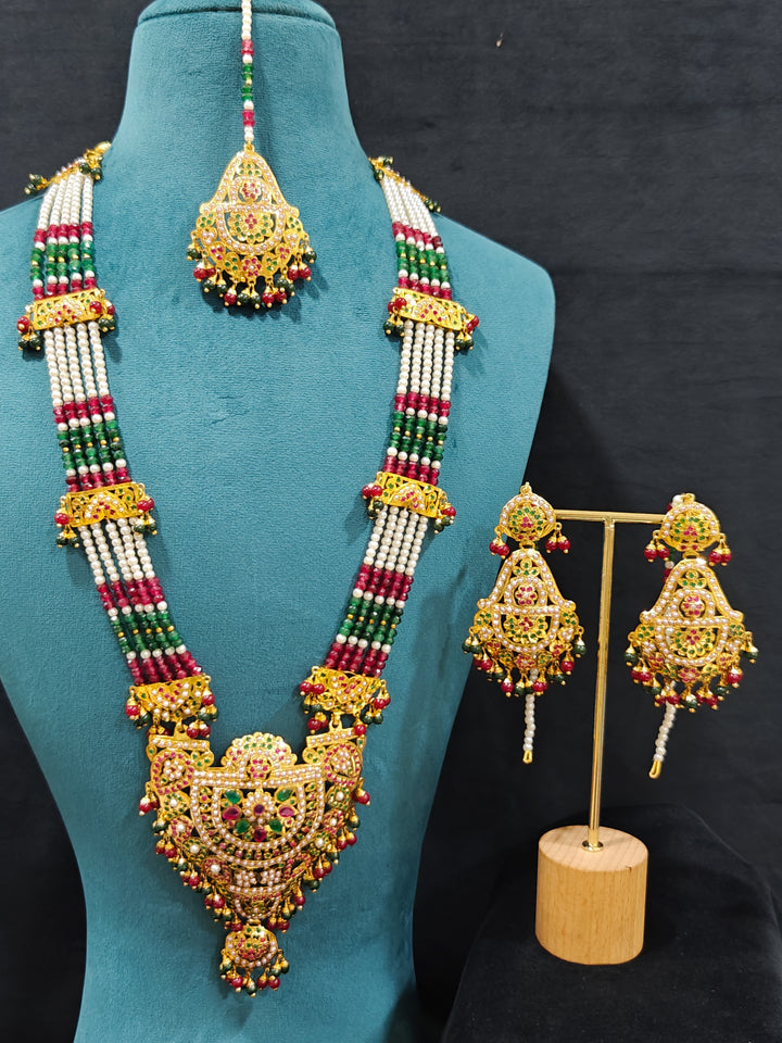 An ornate traditional Long jadau gold jewellery set and  jadau earrings and maangtikka with crystals beads and gemstones. Wedding guest styling a long Jadau artificial necklace. Jadau necklace styled for a wedding guest outfit.

