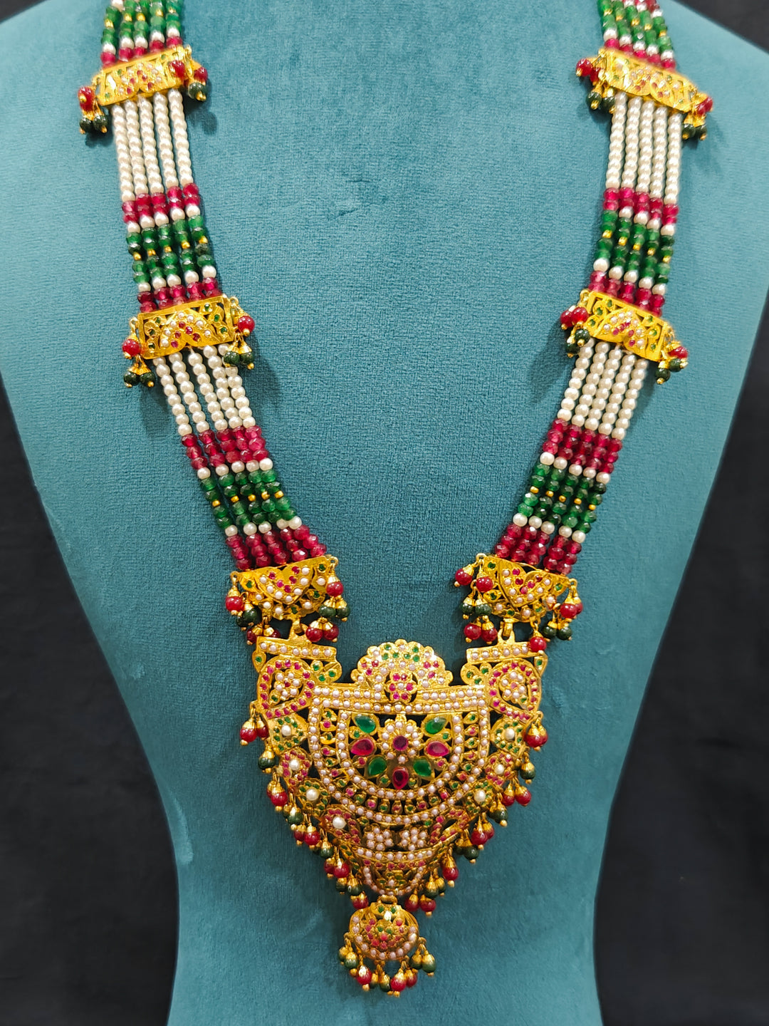 Closeup of an ornate traditional Long jadau gold jewellery set and  jadau earrings and maangtikka with crystals beads and gemstones. Wedding guest styling a long Jadau artificial necklace. Jadau necklace styled for a wedding guest outfit.

