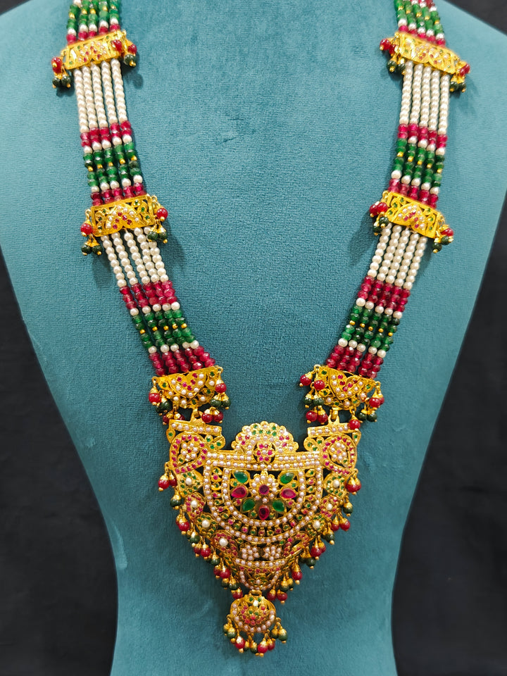 Closeup of an ornate traditional Long jadau gold jewellery set and  jadau earrings and maangtikka with crystals beads and gemstones. Wedding guest styling a long Jadau artificial necklace. Jadau necklace styled for a wedding guest outfit.

