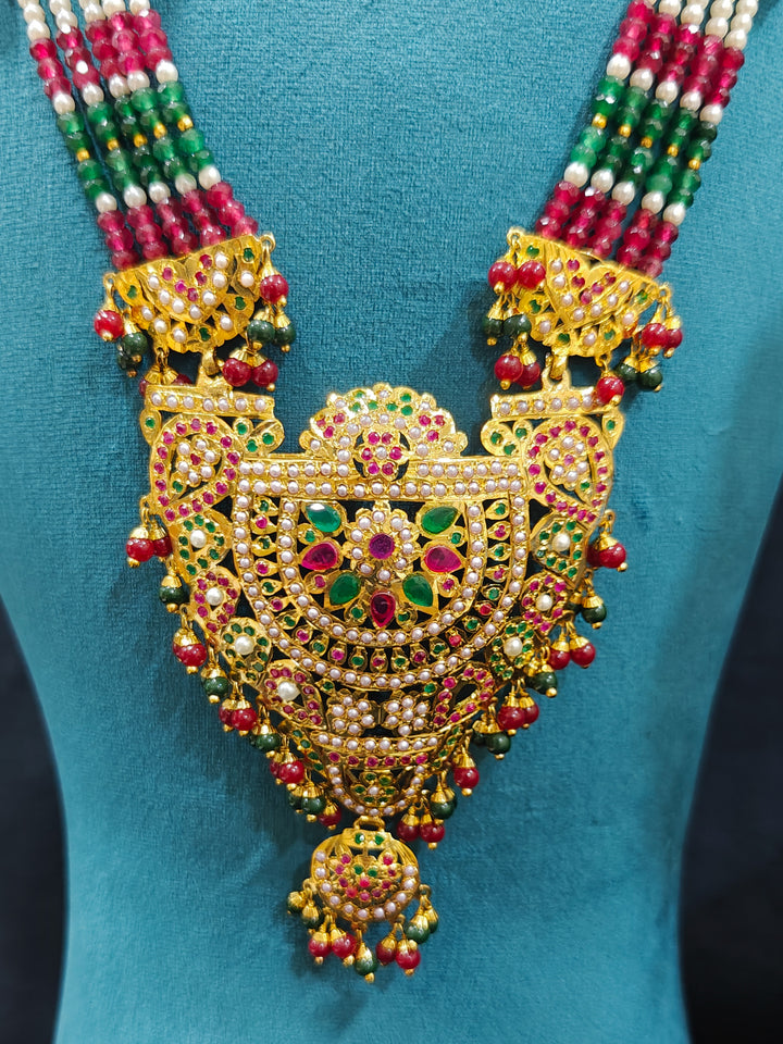 Closeup of an ornate traditional Long jadau gold jewellery set and  jadau earrings and maangtikka with crystals beads and gemstones. Wedding guest styling a long Jadau artificial necklace. Jadau necklace styled for a wedding guest outfit.


