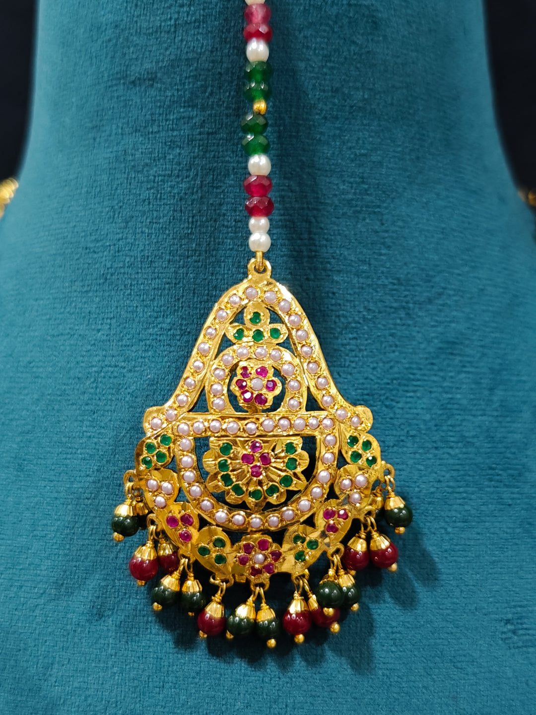 Closeup of an ornate traditional necklace with matched Decorative gold Mangtikka  with crystals beads and gemstones. Wedding guest styling a long Jadau artificial necklace. Jadau necklace styled for a wedding guest outfit.

