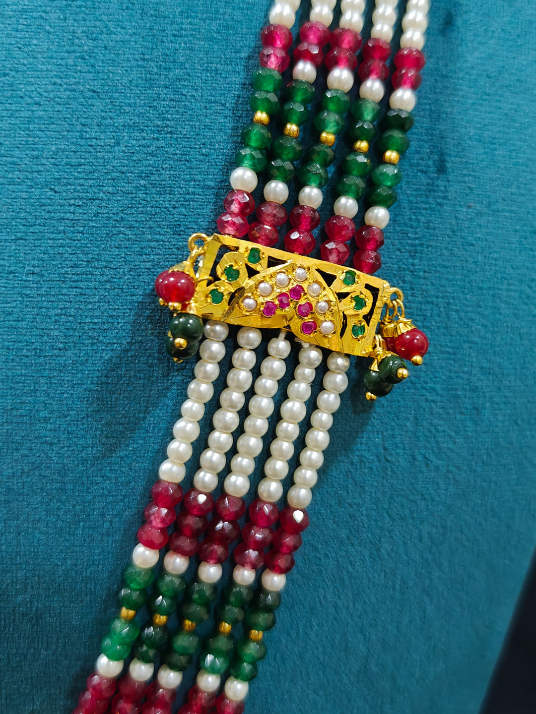 Closeup of an ornate traditional Long jadau gold jewellery set and  jadau earrings and maangtikka with crystals beads and gemstones. Wedding guest styling a long Jadau artificial necklace. Jadau necklace styled for a wedding guest outfit.