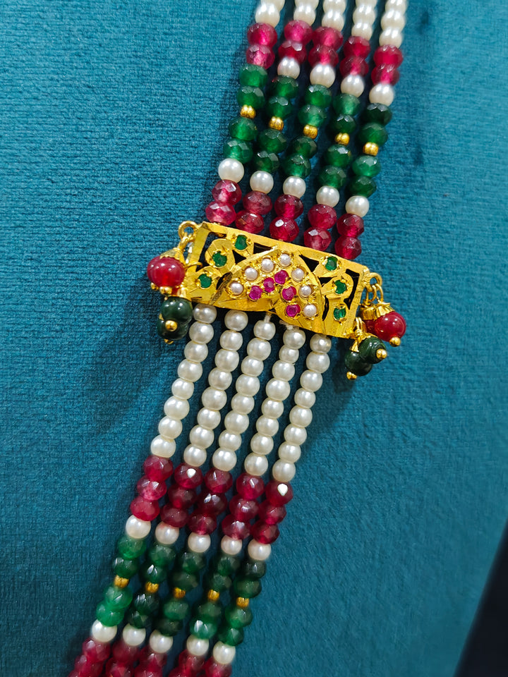 Closeup of an ornate traditional Long jadau gold jewellery set and  jadau earrings and maangtikka with crystals beads and gemstones. Wedding guest styling a long Jadau artificial necklace. Jadau necklace styled for a wedding guest outfit.