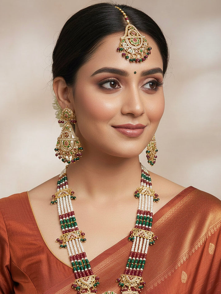 Close-up of a woman wearing an ornate handmade jadau jewelry set and earrings and maangtikka with red and green jadau beads and gemstones. This is a perfect jadau jewelry set for weddings, festivals and more. Can also be worn as bridal jadau jewelry for indian weddings. 