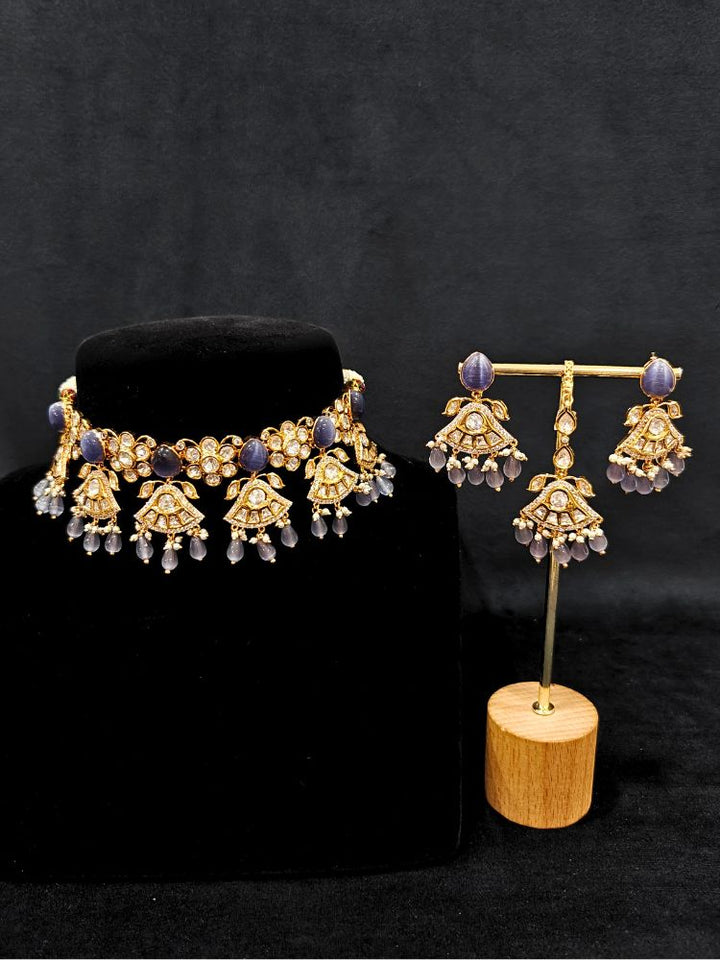 Close-up of an ornate traditional (Gold Polish) Lilac Choker jewellery set and earrings and maangtikka with Polki, Tumble Beads and Lilac Colored Stones. Woman wearing trending Polki artificial jewelry for the wedding season in India. Festive celebration look completed with premium imitation Polki jewelry.