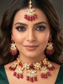 Close-up of a woman wearing an ornate traditional (Gold Polish) Ruby Red Choker jewellery set and earrings and maangtikka with Polki, Tumble Beads and Ruby Red Colored Stones. Woman wearing trending Polki artificial jewelry for the wedding season in India. Festive celebration look completed with premium imitation Polki jewelry.
