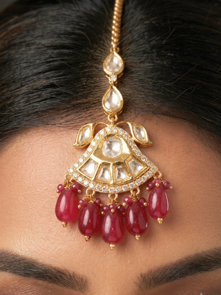 Close-up of a woman wearing an ornate traditional (Gold Polish) Ruby Red Choker jewellery set and earrings and maangtikka with Polki, Tumble Beads and Ruby Red Colored Stones. Woman wearing trending Polki artificial jewelry for the wedding season in India. Festive celebration look completed with premium imitation Polki jewelry.