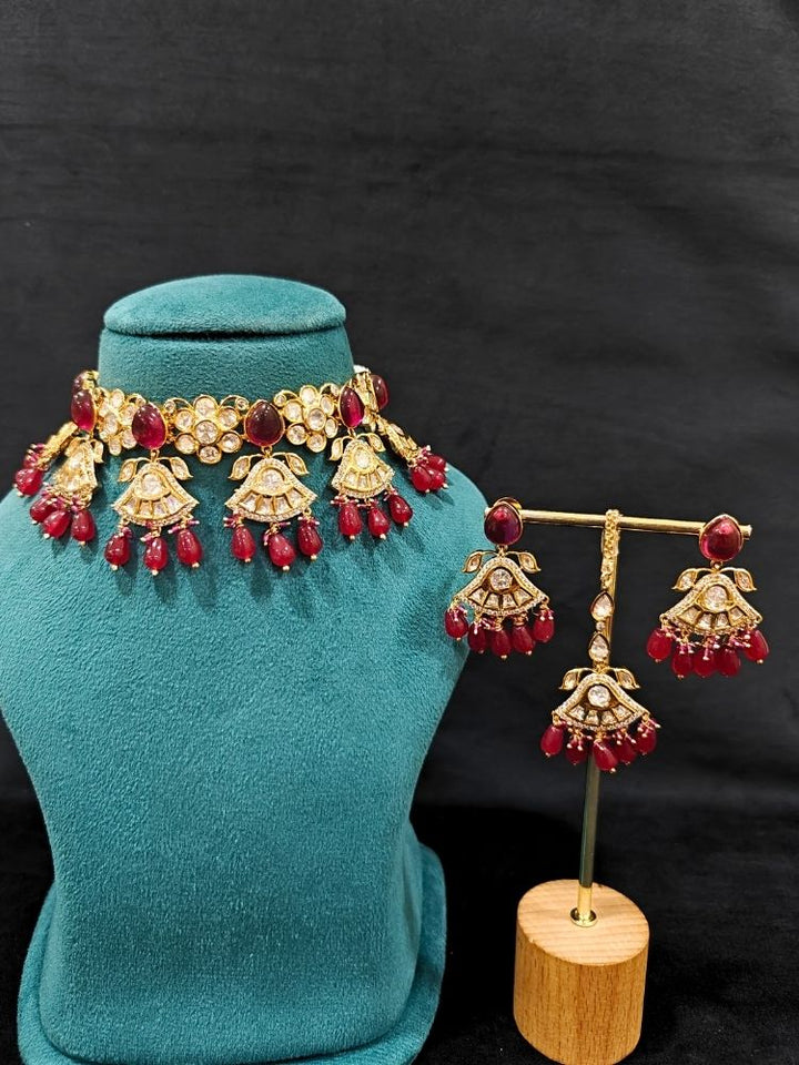 Close-up of an ornate traditional (Gold Polish) Ruby Red Choker jewellery set and earrings and maangtikka with Polki, Tumble Beads and Ruby Red Colored Stones. Woman wearing trending Polki artificial jewelry for the wedding season in India. Festive celebration look completed with premium imitation Polki jewelry.