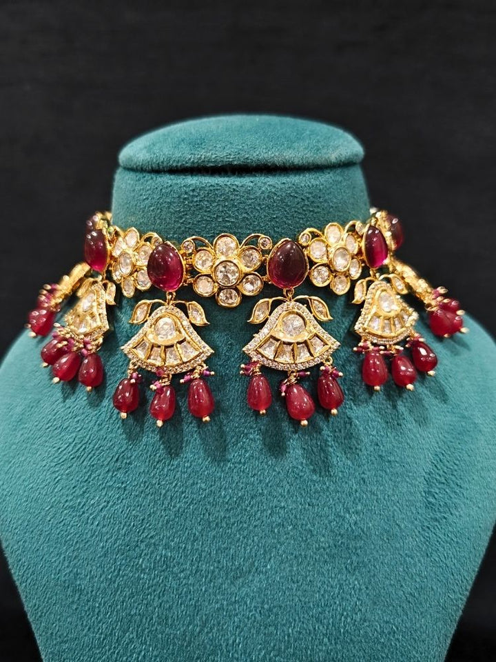 Close-up of an ornate traditional (Gold Polish) Ruby Red Choker jewellery set and earrings and maangtikka with Polki, Tumble Beads and Ruby Red Colored Stones. Woman wearing trending Polki artificial jewelry for the wedding season in India. Festive celebration look completed with premium imitation Polki jewelry.