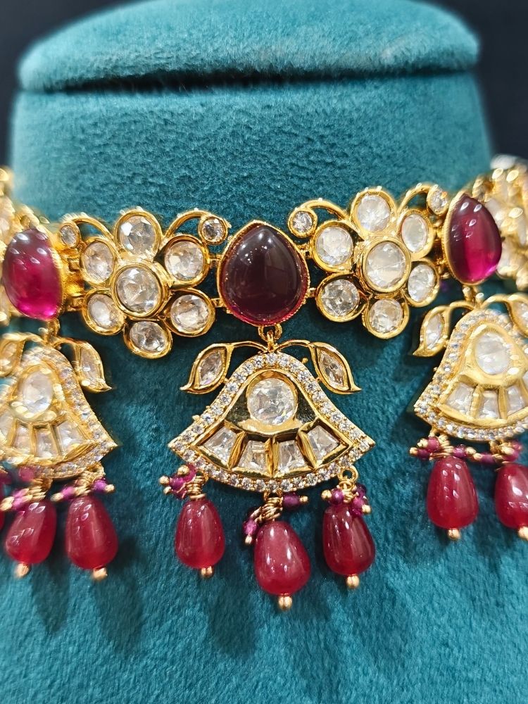 Close-up of an ornate traditional (Gold Polish) Ruby Red Choker jewellery set and earrings and maangtikka with Polki, Tumble Beads and Ruby Red Colored Stones. Woman wearing trending Polki artificial jewelry for the wedding season in India. Festive celebration look completed with premium imitation Polki jewelry.