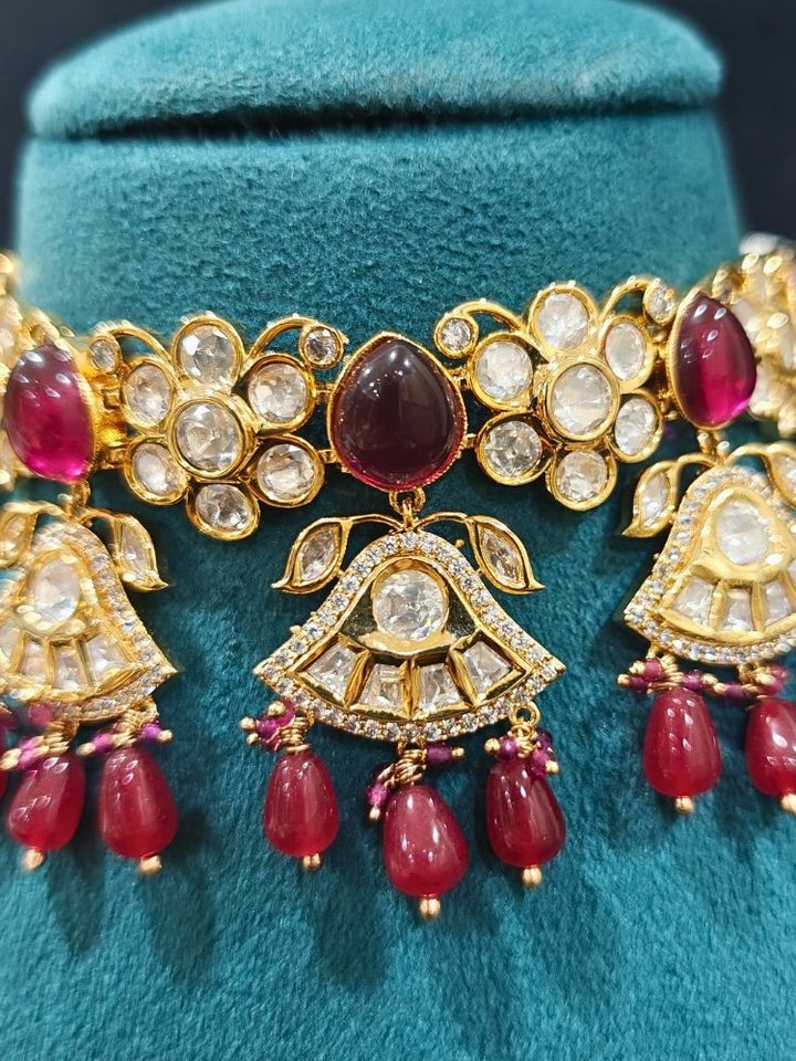 Close-up of an ornate traditional (Gold Polish) Ruby Red Choker jewellery set and earrings and maangtikka with Polki, Tumble Beads and Ruby Red Colored Stones. Woman wearing trending Polki artificial jewelry for the wedding season in India. Festive celebration look completed with premium imitation Polki jewelry.