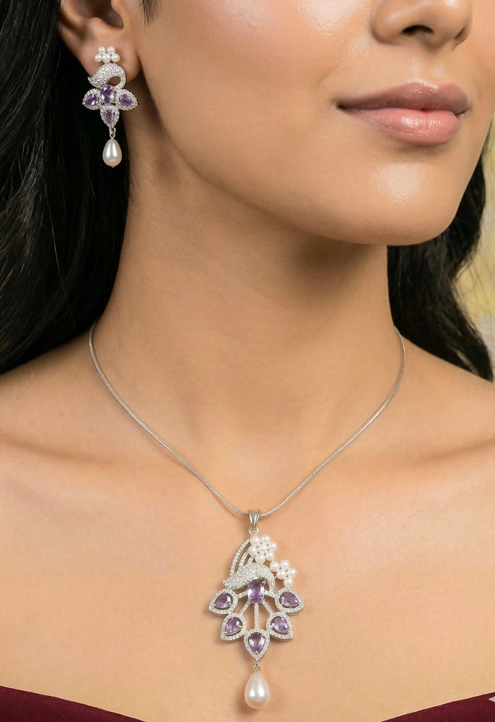 Close-up of a woman wearing an ornate Indo-western Purple (Silver Polish)  Pendant set and earrings with American Diamonds, Colored Stones and Pearls. Woman styling a statement American diamond Pendant with an off-shoulder gown for a reception. Indo-western outfit styled with a statement American diamond Pendant set.
