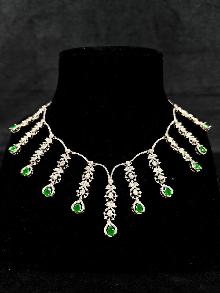  A gorgeous artificial diamond and green colored stone necklace paired with diamond earrings. This artificial diamond jewelry set offers a traditional yet modern touch for Indian brides, designed to add elegance and sophistication to any occasion.