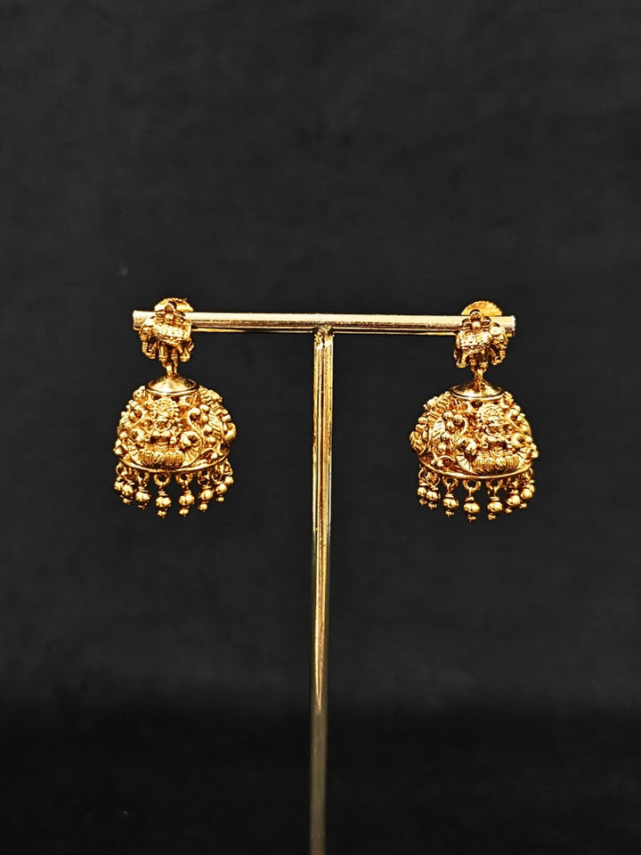 The Ambhira Laxmi Hasli Necklace Set featuring a traditional gold Collar Hasli necklace and matching earrings with Goddess Laxmi in the middle, along with American Diamonds and Colored Stones. Wedding guest look completed with a Hasli temple necklace set.