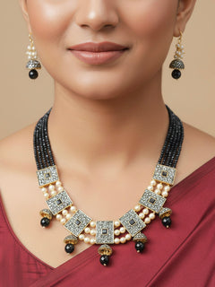 Close-up of a woman wearing an ornate traditional Black Collar jewellery set and earrings with Black Crystals Beads, Pearls, Chatten Squares and Colored Stones. Mehendi ceremony look completed with a handcrafted Pearl jewelry set. Bride showcasing a traditional Pearl artificial jewelry set in India.