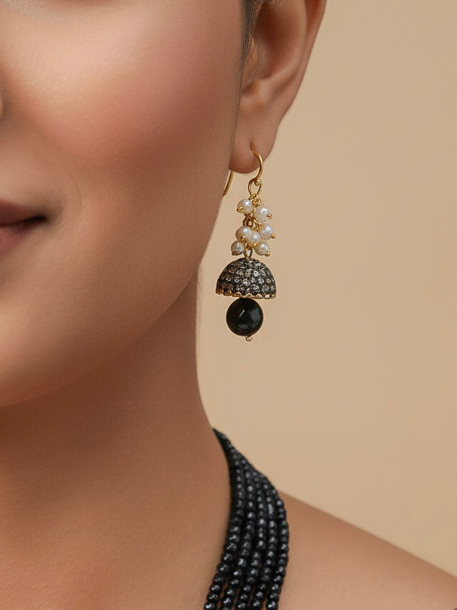 Close-up of a woman wearing an ornate traditional Black Collar jewellery set and earrings with Black Crystals Beads, Pearls, Chatten Squares and Colored Stones. Mehendi ceremony look completed with a handcrafted Pearl jewelry set. Bride showcasing a traditional Pearl artificial jewelry set in India.