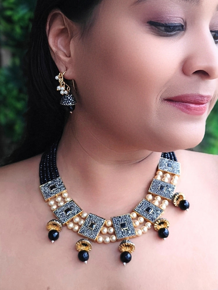 Close-up of a woman wearing an ornate traditional Black Collar jewellery set and earrings with Black Crystals Beads, Pearls, Chatten Squares and Colored Stones. Mehendi ceremony look completed with a handcrafted Pearl jewelry set. Bride showcasing a traditional Pearl artificial jewelry set in India.