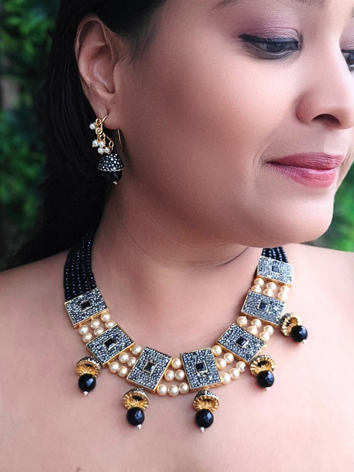 Close-up of a woman wearing an ornate traditional Black Collar jewellery set and earrings with Black Crystals Beads, Pearls, Chatten Squares and Colored Stones. Mehendi ceremony look completed with a handcrafted Pearl jewelry set. Bride showcasing a traditional Pearl artificial jewelry set in India.