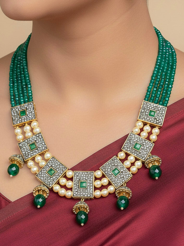 Close-up of a woman wearing an ornate traditional Dark Green Collar jewellery set and earrings with Dark Green Crystals Beads, Pearls, Chatten Squares and Colored Stones. Mehendi ceremony look completed with a handcrafted Pearl jewelry set. Bride showcasing a traditional Pearl artificial jewelry set in India.