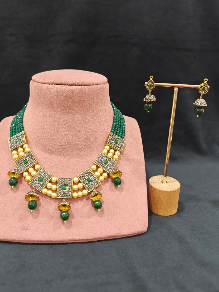 Close-up of an ornate traditional Dark Green Collar jewellery set and earrings with Dark Green Crystals Beads, Pearls, Chatten Squares and Colored Stones. Mehendi ceremony look completed with a handcrafted Pearl jewelry set. Bride showcasing a traditional Pearl artificial jewelry set in India.