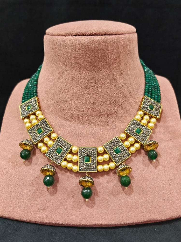 Close-up of an ornate traditional Dark Green Collar jewellery set and earrings with Dark Green Crystals Beads, Pearls, Chatten Squares and Colored Stones. Mehendi ceremony look completed with a handcrafted Pearl jewelry set. Bride showcasing a traditional Pearl artificial jewelry set in India.