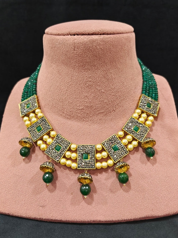 Close-up of an ornate traditional Dark Green Collar jewellery set and earrings with Dark Green Crystals Beads, Pearls, Chatten Squares and Colored Stones. Mehendi ceremony look completed with a handcrafted Pearl jewelry set. Bride showcasing a traditional Pearl artificial jewelry set in India.