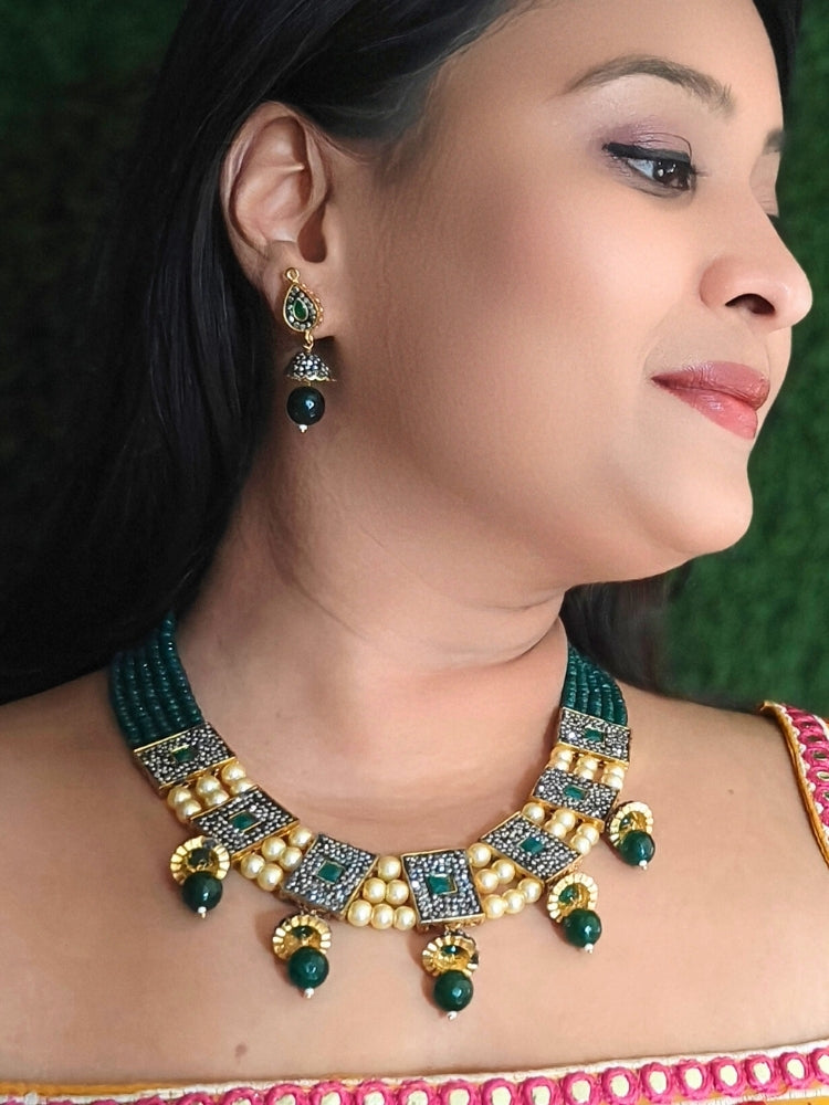 Close-up of a woman wearing an ornate traditional Dark Green Collar jewellery set and earrings with Dark Green Crystals Beads, Pearls, Chatten Squares and Colored Stones. Mehendi ceremony look completed with a handcrafted Pearl jewelry set. Bride showcasing a traditional Pearl artificial jewelry set in India.