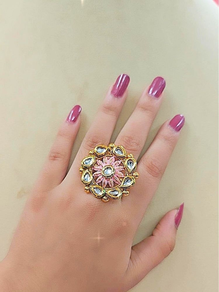 The Anamika Pink Kundan Ring is a round, ornate gold adjustable ring with teardrop-shaped white Kundan stones and Pink enamel, shown on a girls hand with pink nail paint. 