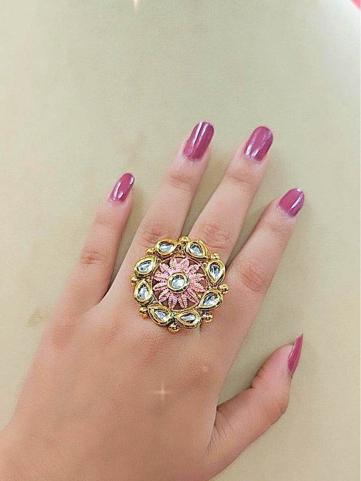 The Anamika Pink Kundan Ring is a round, ornate gold adjustable ring with teardrop-shaped white Kundan stones and Pink enamel, shown on a girls hand with pink nail paint. 