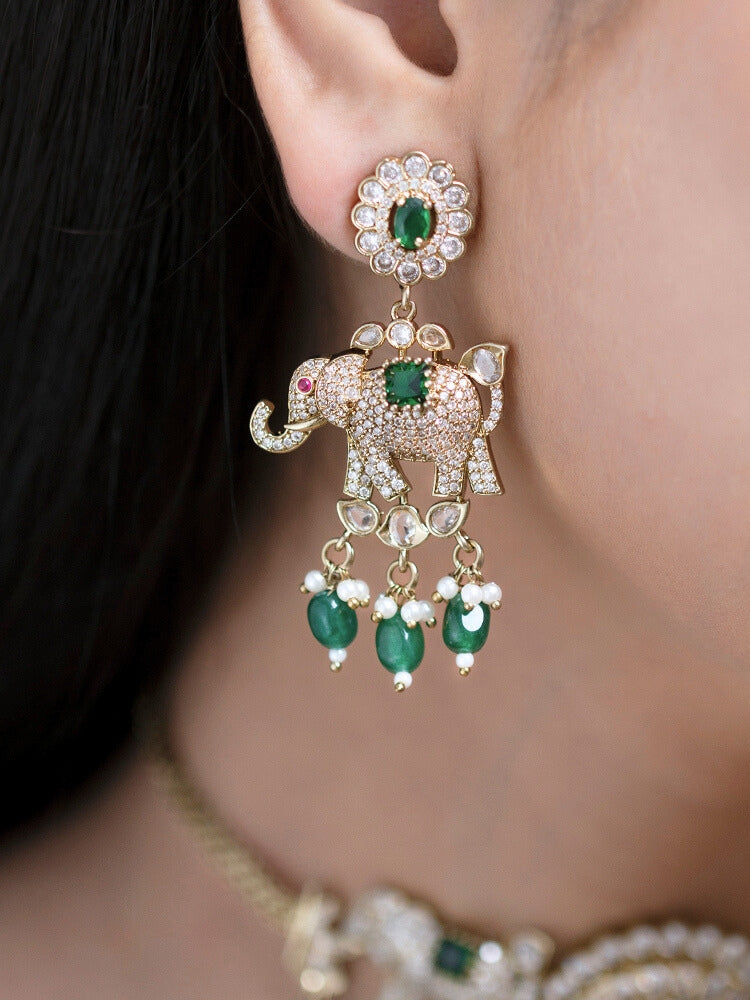 A woman wearing the Aneya Dark Green Choker Necklace Set, featuring ornate gold-toned jewelry with Dark Green and white colored stones and elephant-shaped motifs in the necklace and earrings, poses in traditional attire, her long dark hair partially visible.