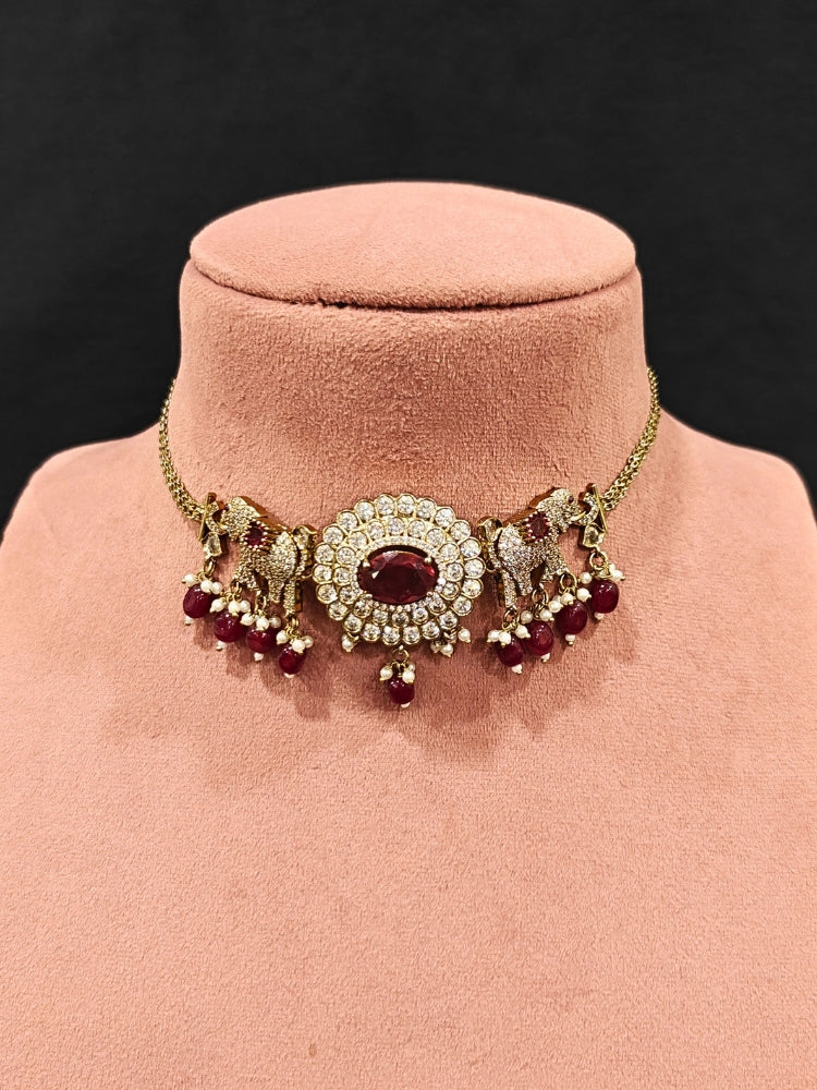 Close-up of an ornate traditional Maroon (Mehendi gold Polish) Choker Diamond jewellery set and earrings with American Diamond, Pearls and Colored Stone. Elegant festive look with a high-quality imitation American diamond necklace set. A luxury American diamond necklace set styled beautifully for a wedding guest look in India.