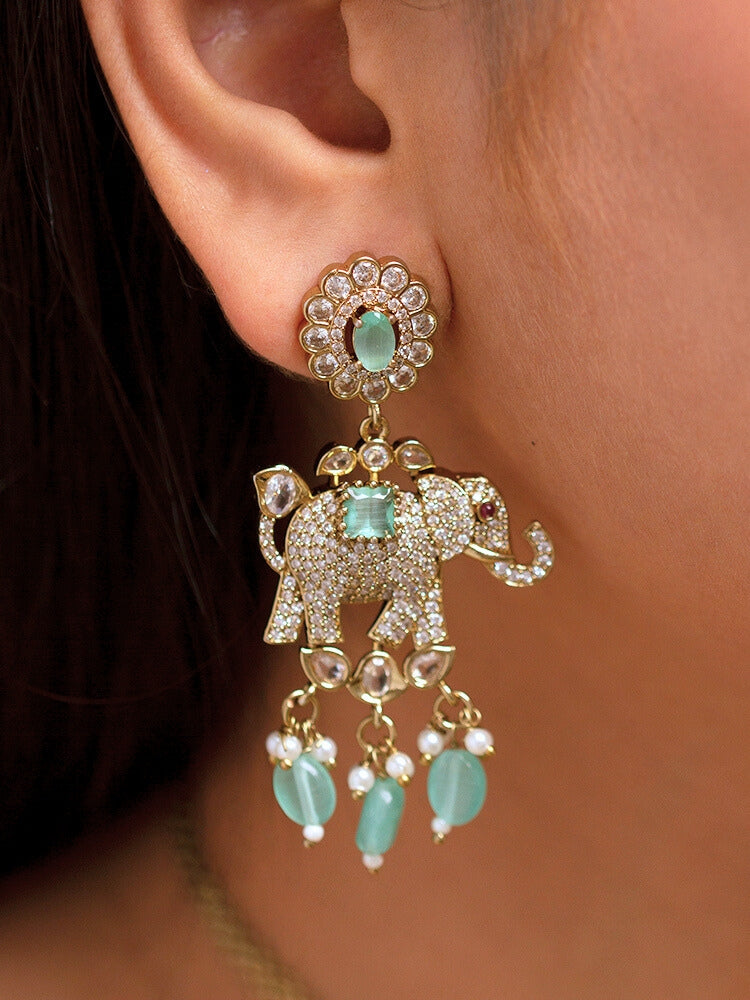 A woman wearing the Aneya Mint Green Choker Necklace Set, featuring ornate gold-toned jewelry with Mint Green and white colored stones and elephant-shaped motifs in the necklace and earrings, poses in traditional attire, her long dark hair partially visible.