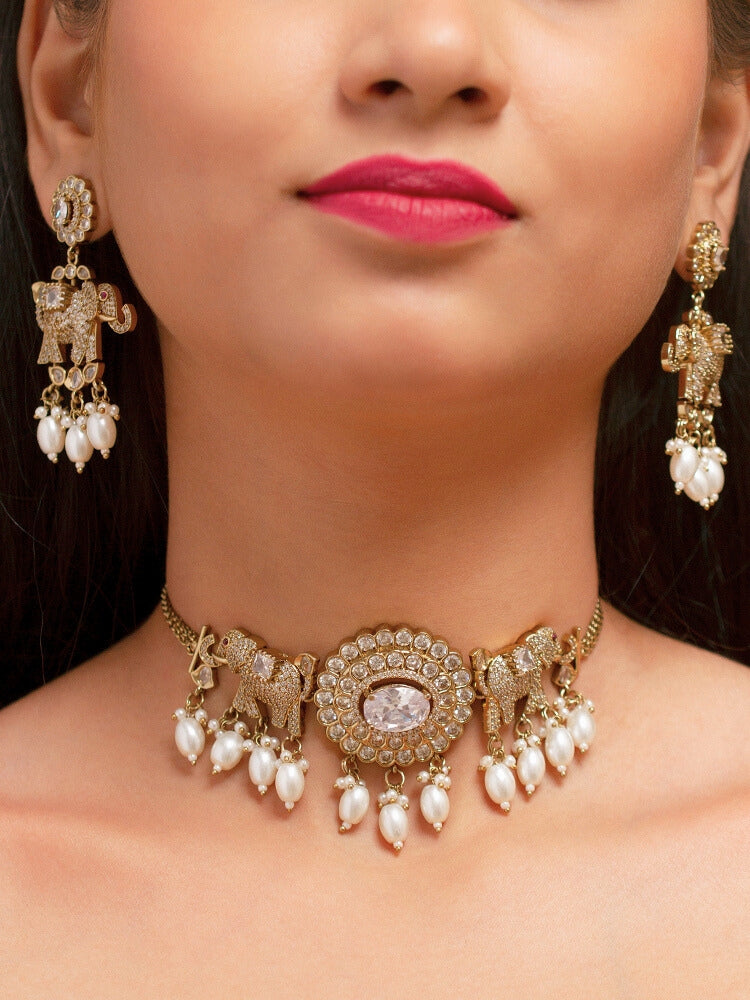 A woman wearing the Aneya White  Choker Necklace Set, featuring ornate gold-toned jewelry with white colored stones and elephant-shaped motifs in the necklace and earrings, poses in traditional attire, her long dark hair partially visible.
