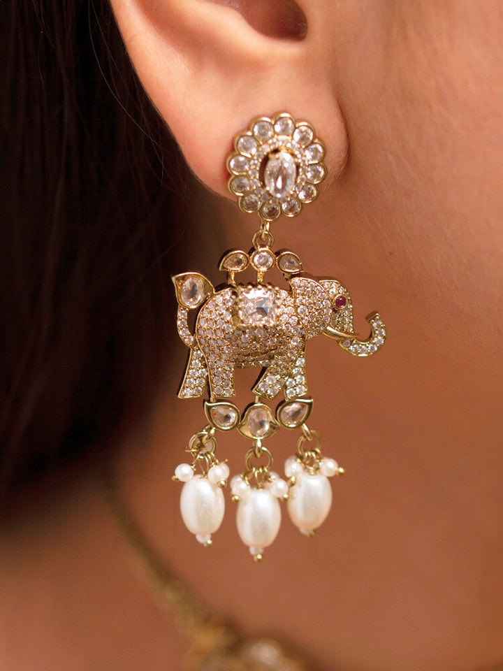 A woman wearing the Aneya White  Choker Necklace Set, featuring ornate gold-toned jewelry with white colored stones and elephant-shaped motifs in the necklace and earrings, poses in traditional attire, her long dark hair partially visible.
