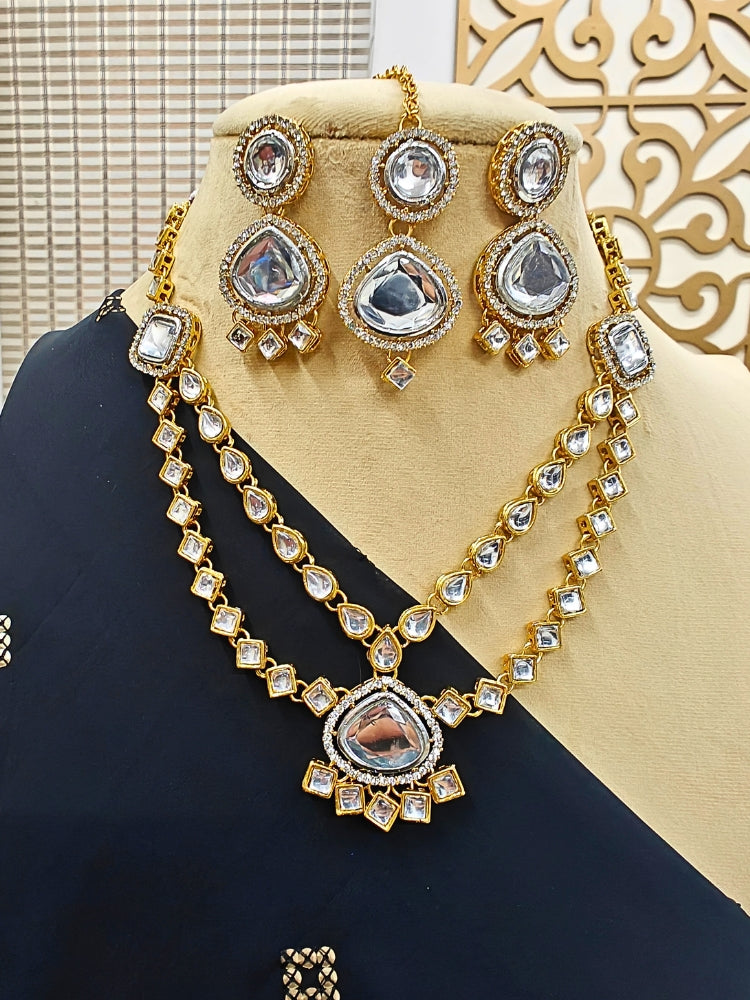 The Anika Necklace Set features gold and white Kundan, with two layered necklace and matching oversized earrings along with a maantikka —displayed on a mannequin in a black saree, its the perfect accent for your wedding ceremony dress.