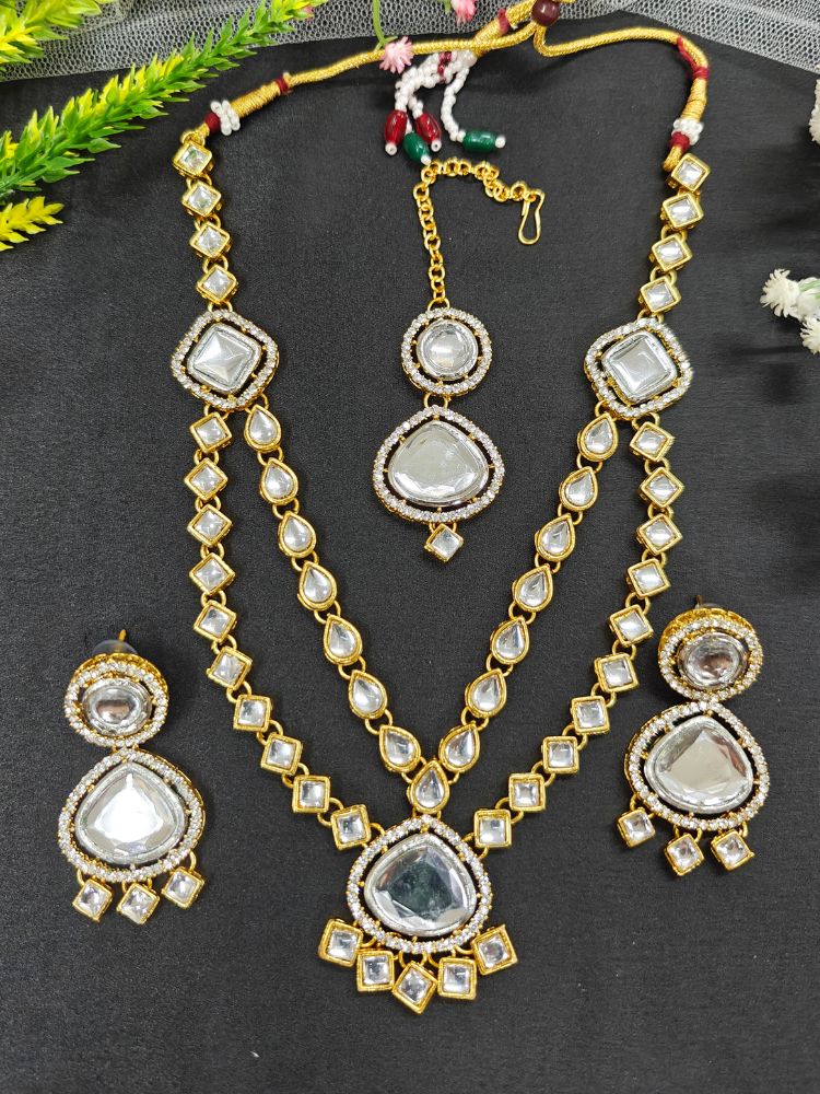 The Anika Necklace Set features gold and white Kundan, with two layered necklace and matching oversized earrings along with a maantikka —displayed on a black Surface, its the perfect accent for your wedding ceremony dress.