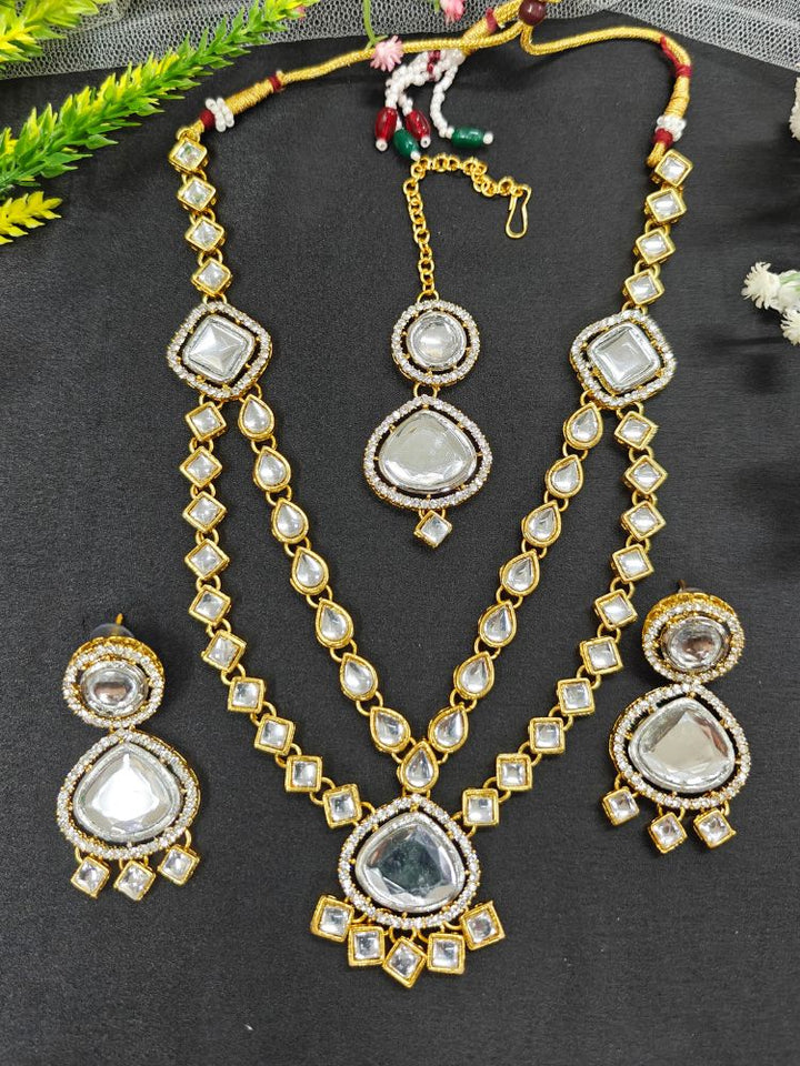 The Anika Necklace Set features gold and white Kundan, with two layered necklace and matching oversized earrings along with a maantikka —displayed on a black Surface, its the perfect accent for your wedding ceremony dress.