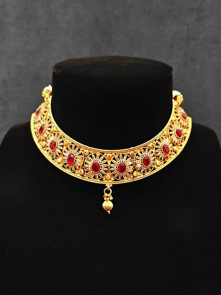Close-up of an ornate traditional Red Diamond gold Polish Choker jewellery set and earrings and maangtikka with Baguette American Diamonds and Red Colored Stones. A luxury American diamond necklace set styled beautifully for a wedding guest look in India. Close-up of a featuring an anti-tarnish American diamond artificial necklace.